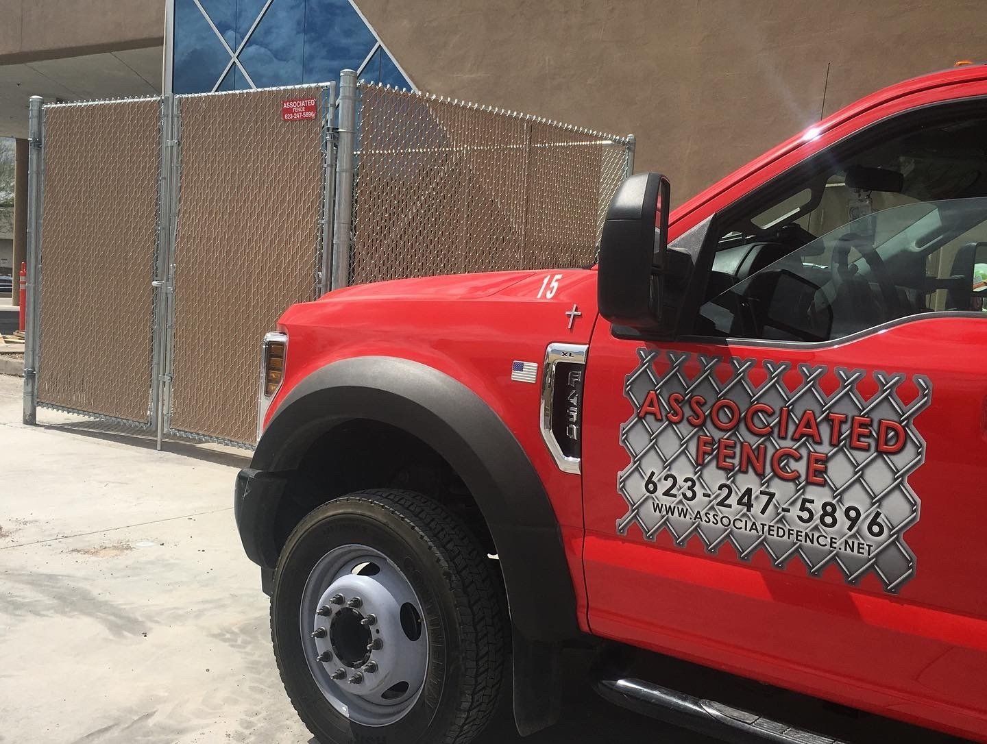 Red Associated Fence truck parked next to a tan privacy fence with a building in the background.