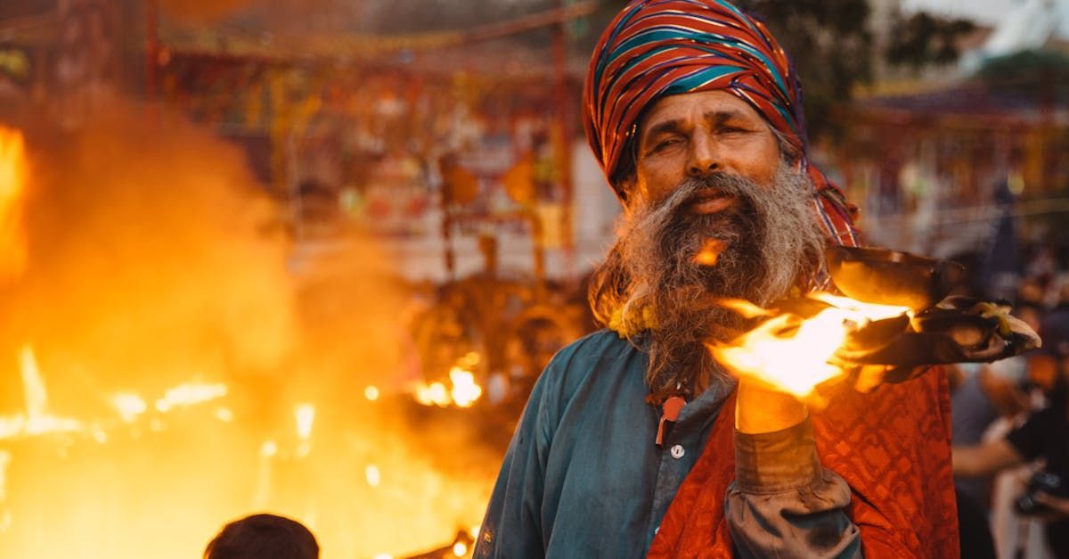 Man with long beard and turban holds fire, outdoors at festival.
