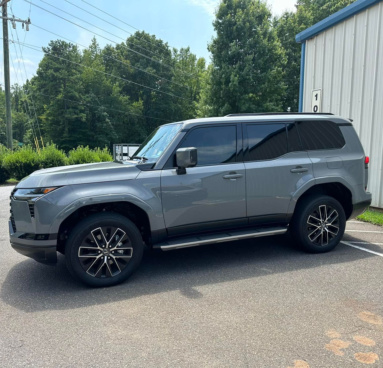 A grey Toyota Land Cruiser parked outdoors on a paved lot beside a white metal building.