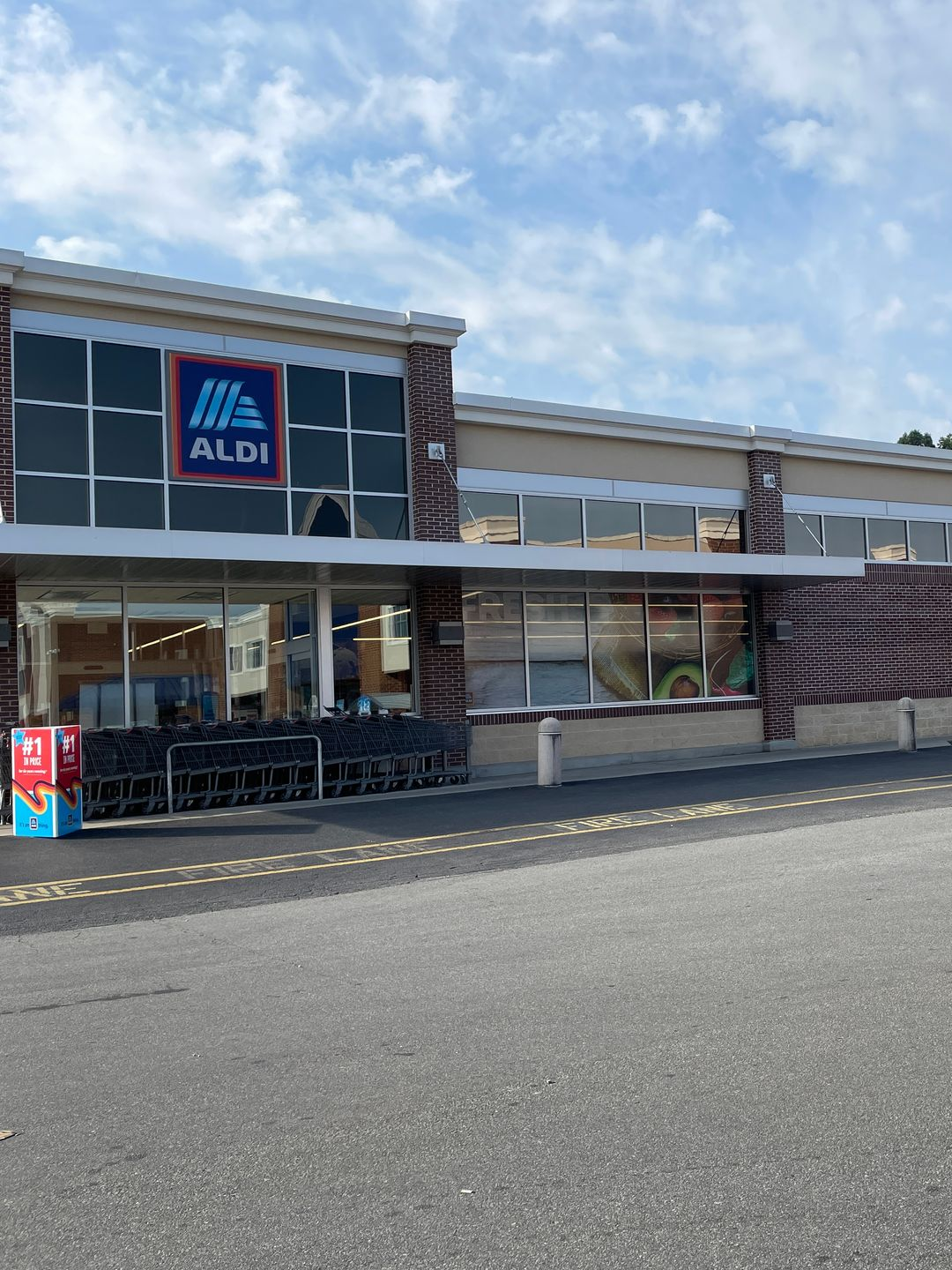 The storefront of an ALDI grocery store with a glass entrance, brick columns, and a parking lot in the foreground.