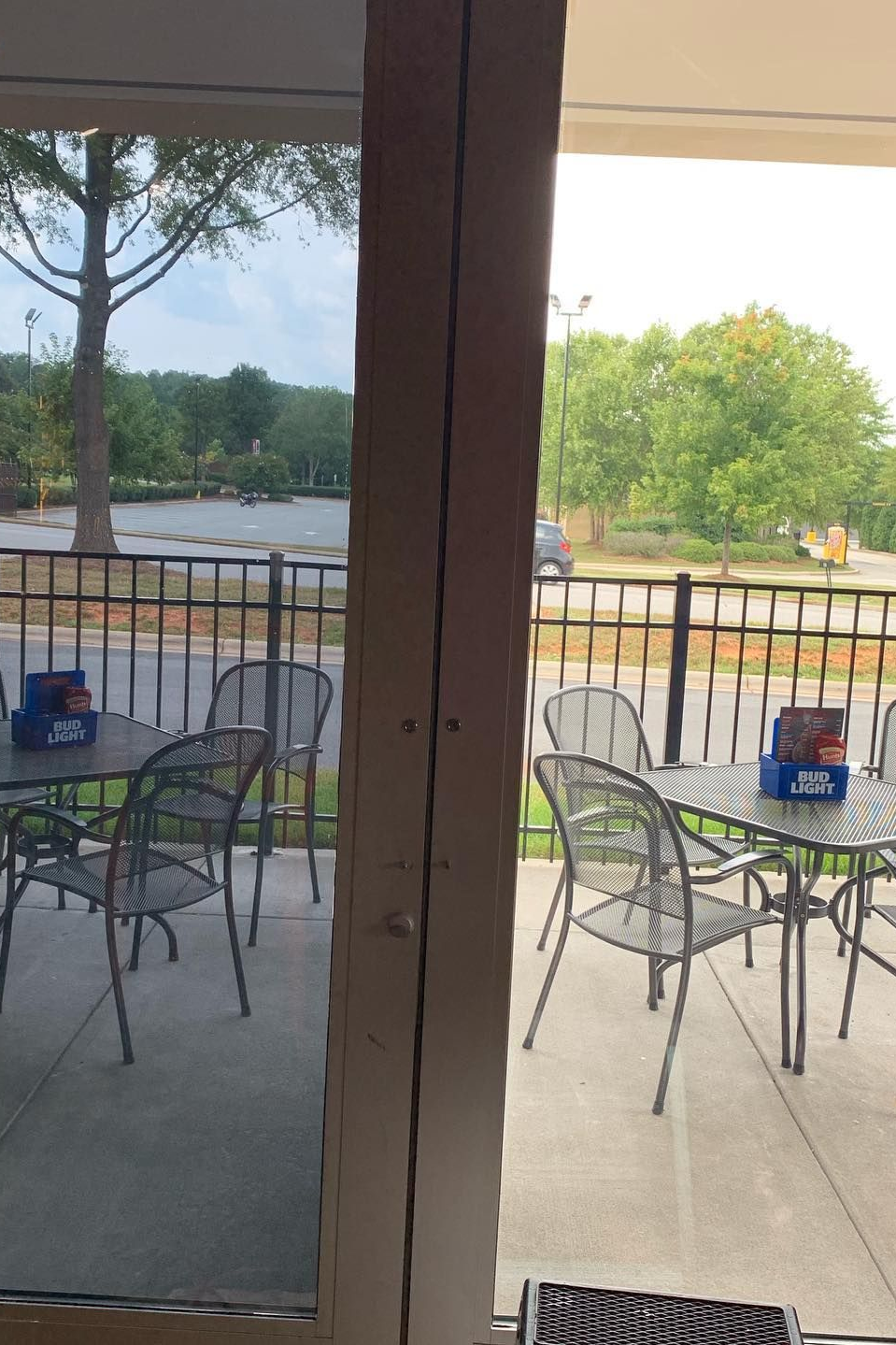 A patio area with outdoor tables and metal chairs, viewed from inside through a window divided by a vertical wooden post.