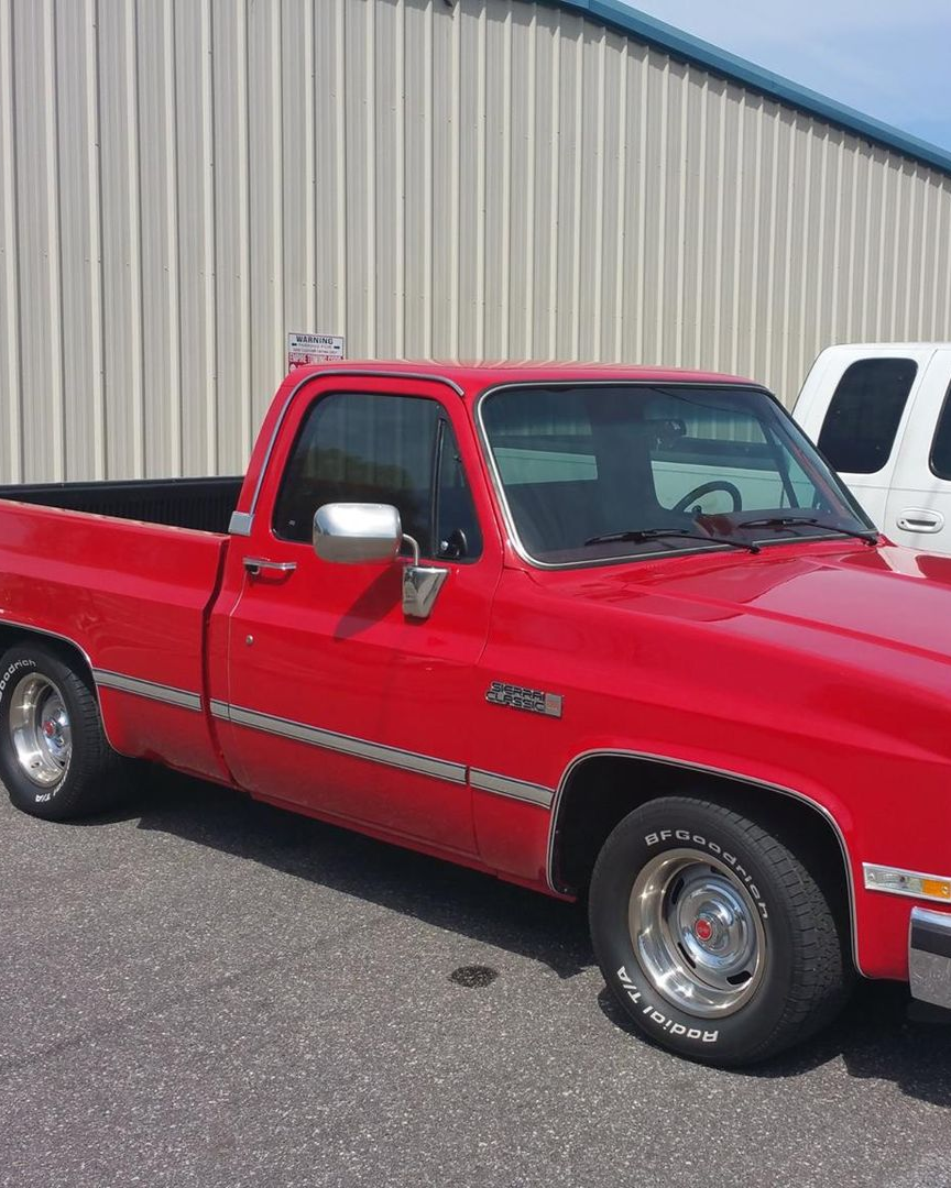 A red, regular-cab Chevrolet C/K pickup truck parked in front of a tan industrial building.
