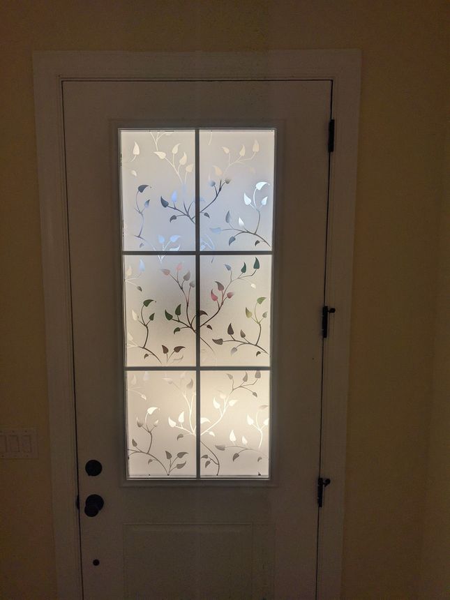 A white door with a central rectangular glass panel featuring a frosted leaf-patterned design.