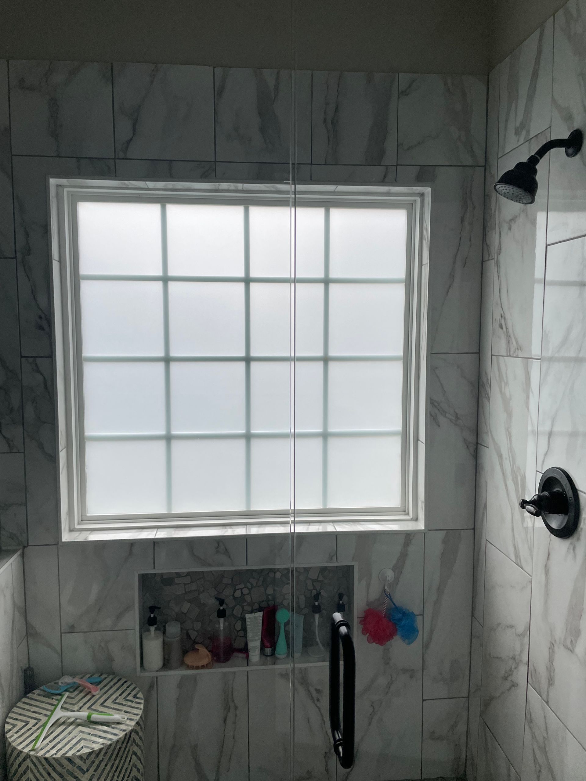 A person standing on an A-frame ladder, using a squeegee to clean a tall, multi-pane window.