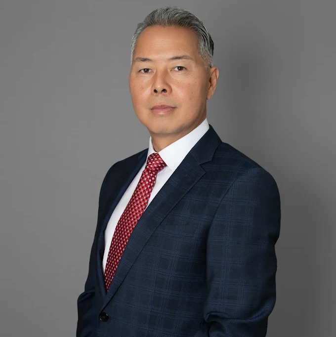 Man in a navy blue suit and red tie, set against a gray background.