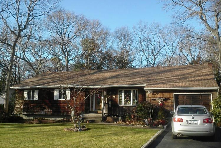 A white car is parked in front of a brown house