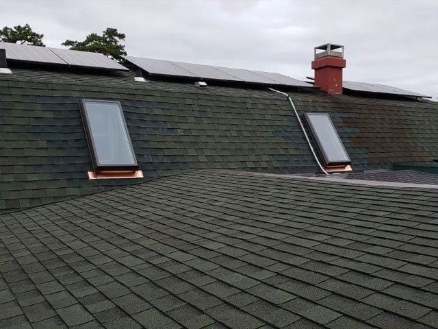A roof with two skylights and solar panels on it.