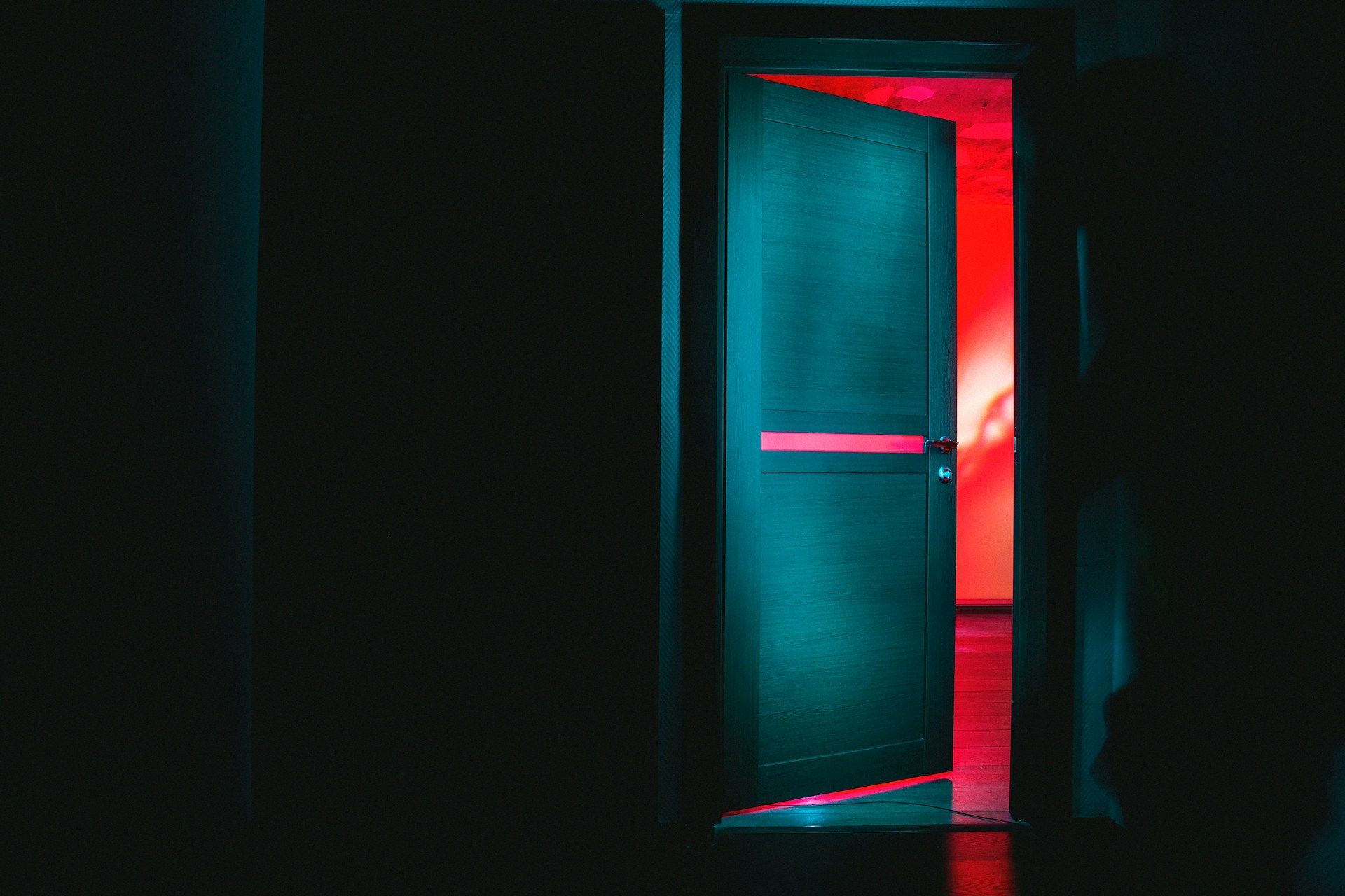 Una puerta está abierta en una habitación oscura de la que sale una luz roja.