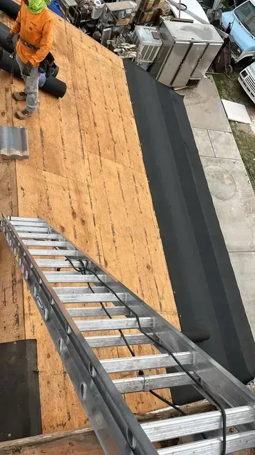 A man is standing on a roof with a ladder attached to it.