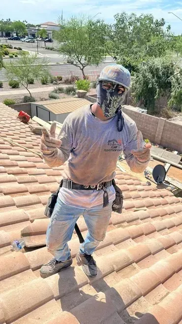 A man wearing a mask is standing on top of a tiled roof giving a thumbs up.