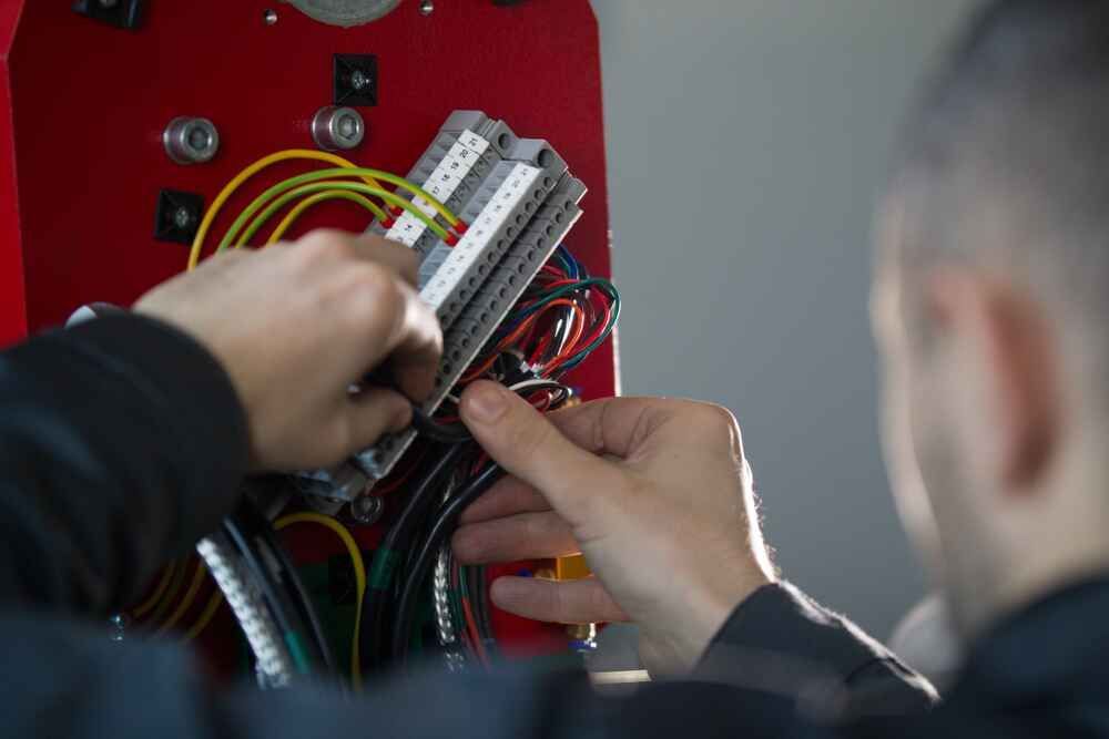 A Man Is Working On A Machine With Wires And Connectors — Bastion Electrical In Wollongong, NSW
