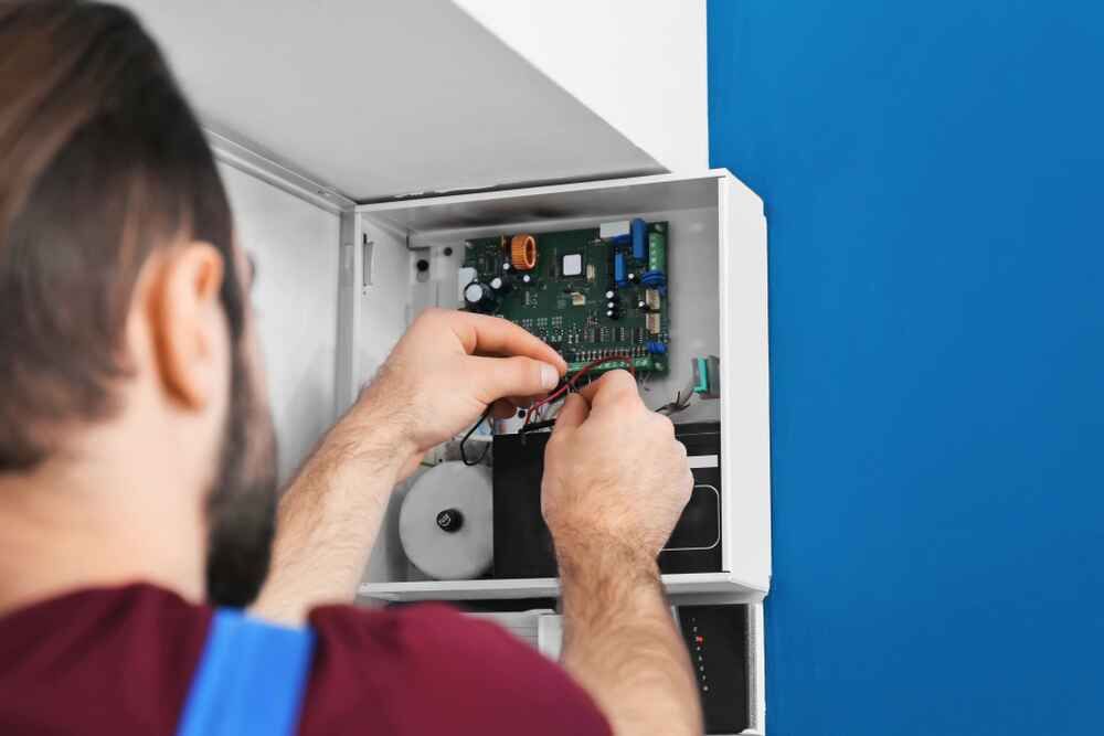 A Man Is Fixing A Security System With A Screwdriver — Bastion Electrical In Shellharbour, NSW