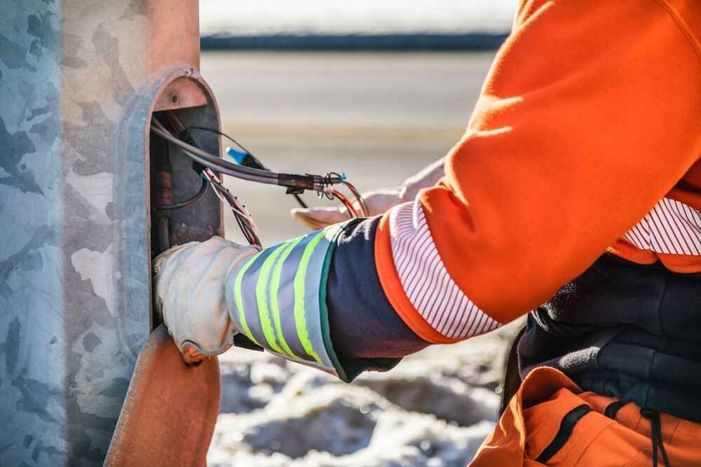 A Man Wearing Safety Gloves Is Working On A Pole — Bastion Electrical In Wollongong, NSW
