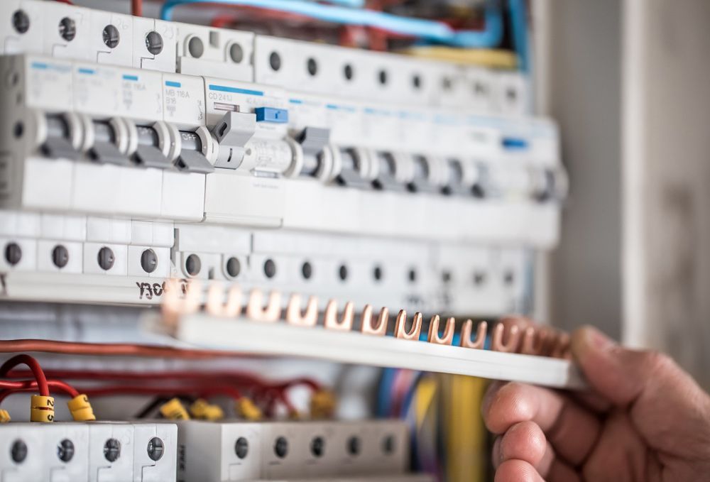 A Person Is Holding A Wire In Front Of An Electrical Box — Bastion Electrical In Wollongong, NSW