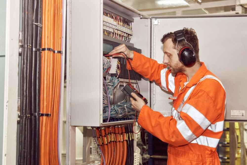 A Man Wearing Headphones Is Working On An Electrical Box — Bastion Electrical In Wollongong, NSW
