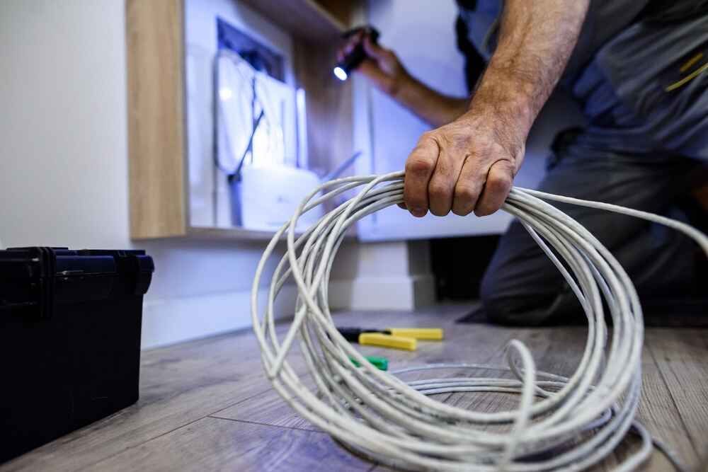 A Man Is Kneeling Down On The Floor Holding A Roll Of Wire — Bastion Electrical In Wollongong, NSW
