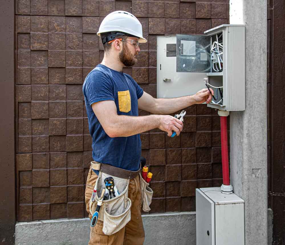 A Man Is Working On An Electrical Box With A Pair Of Pliers — Bastion Electrical In Fairy Meadow, NSW
