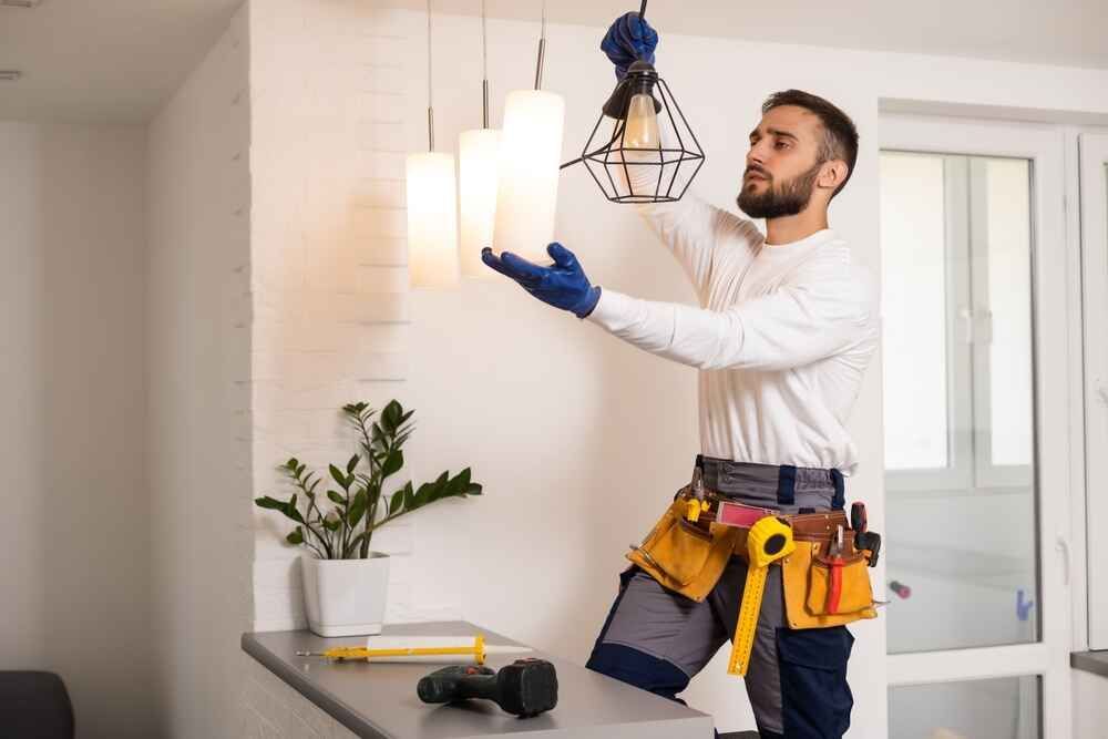 A Man Is Fixing A Light Fixture In A Living Room — Bastion Electrical In Wollongong, NSW
