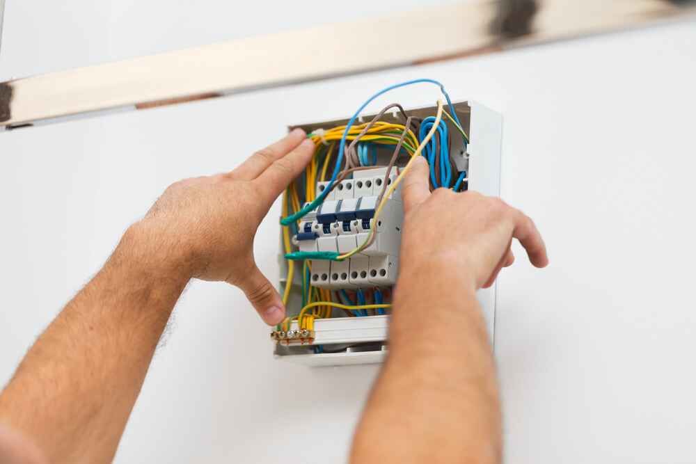 A Man Is Installing An Electrical Box On A Wall — Bastion Electrical In Bulli, NSW

