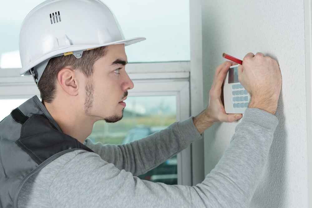 A Man Wearing A Hard Hat Is Installing A Thermostat — Bastion Electrical In Wollongong, NSW
