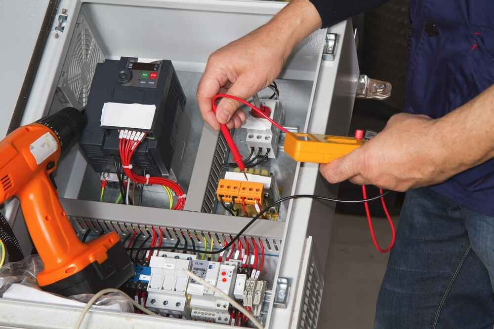A Man Is Working On An Electrical Box With A Drill And A Multimeter — Bastion Electrical In Wollongong, NSW
