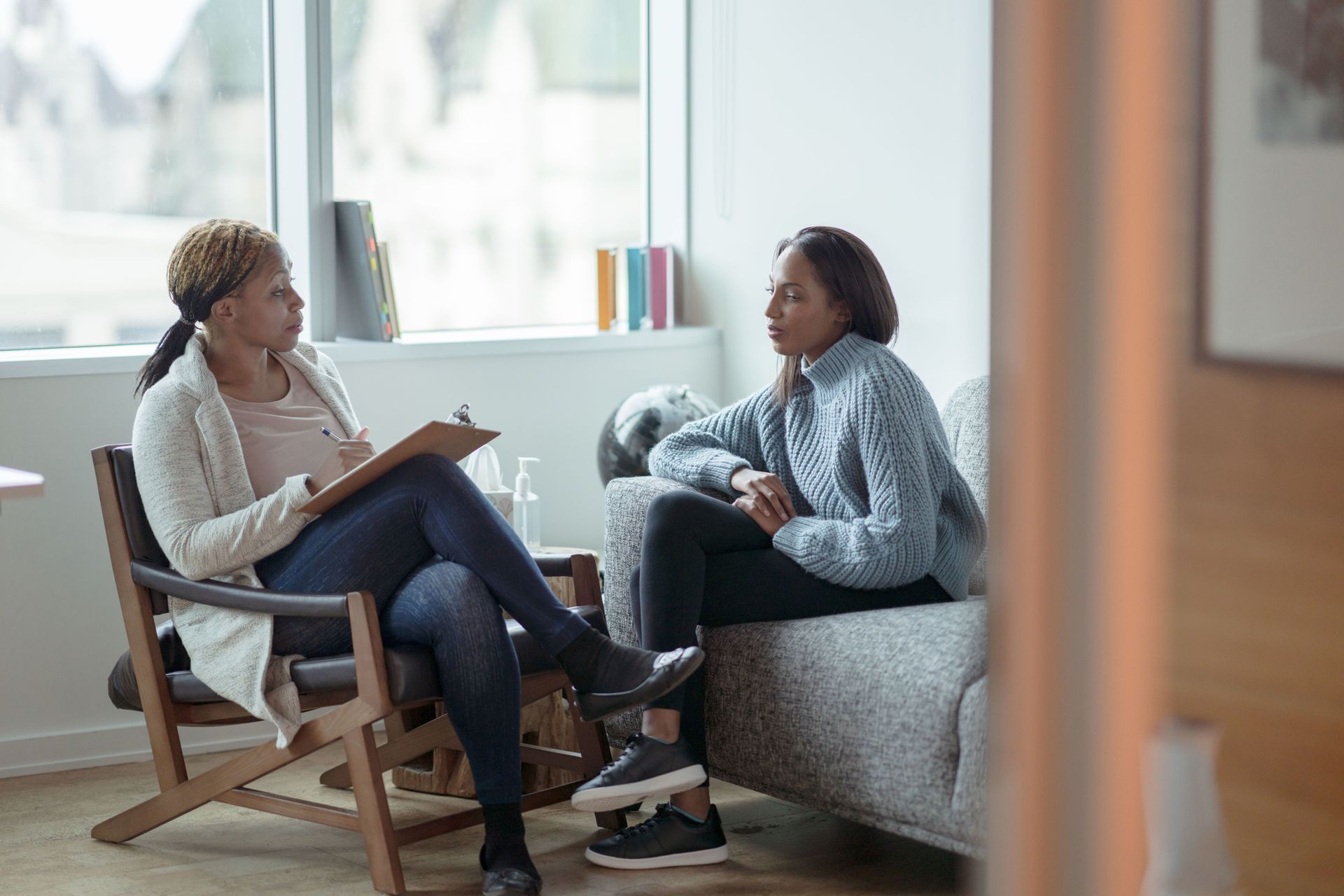 A woman is sitting in a chair talking to another woman on a couch.