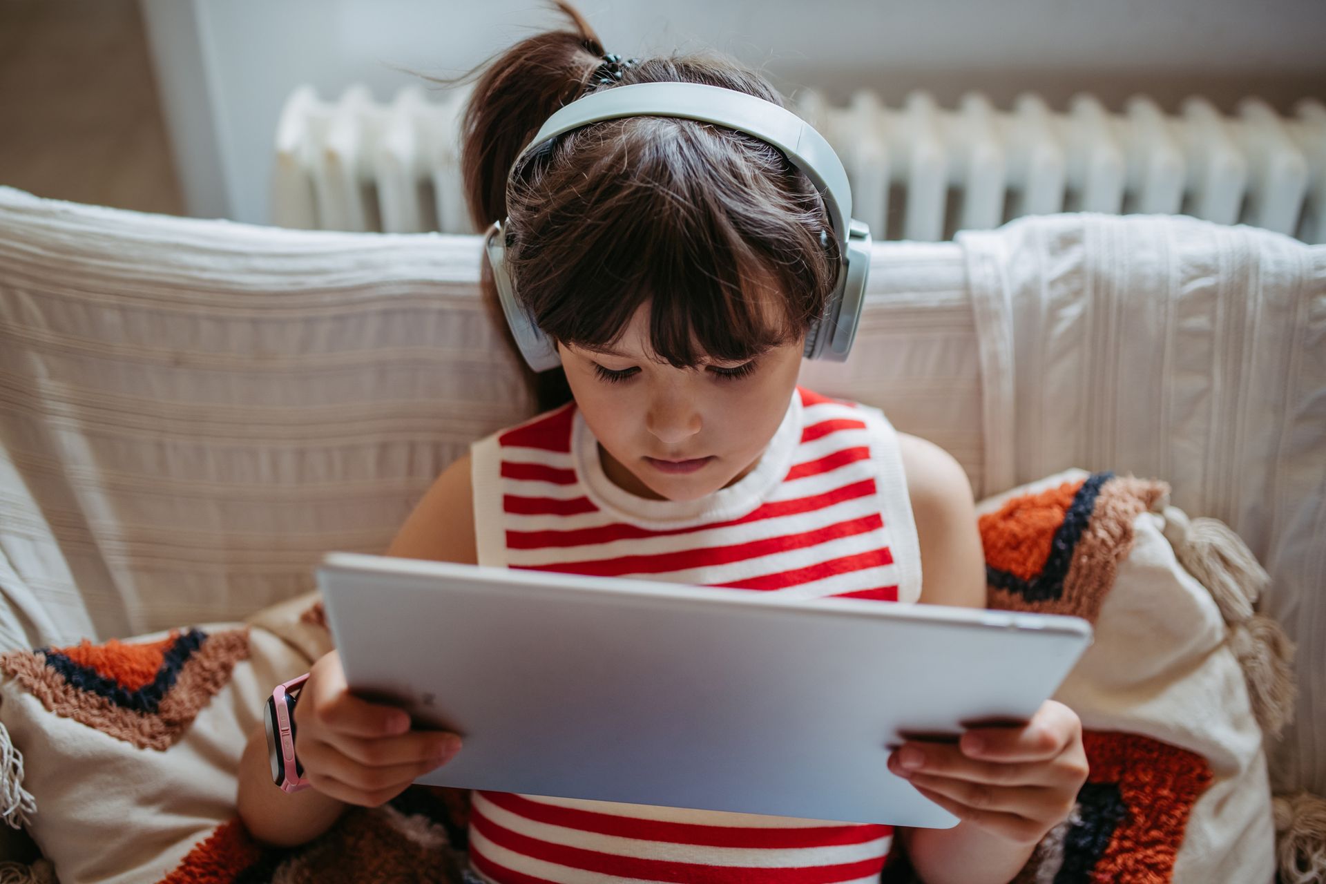A young girl is watching a video on a tablet with wireless headphones on.