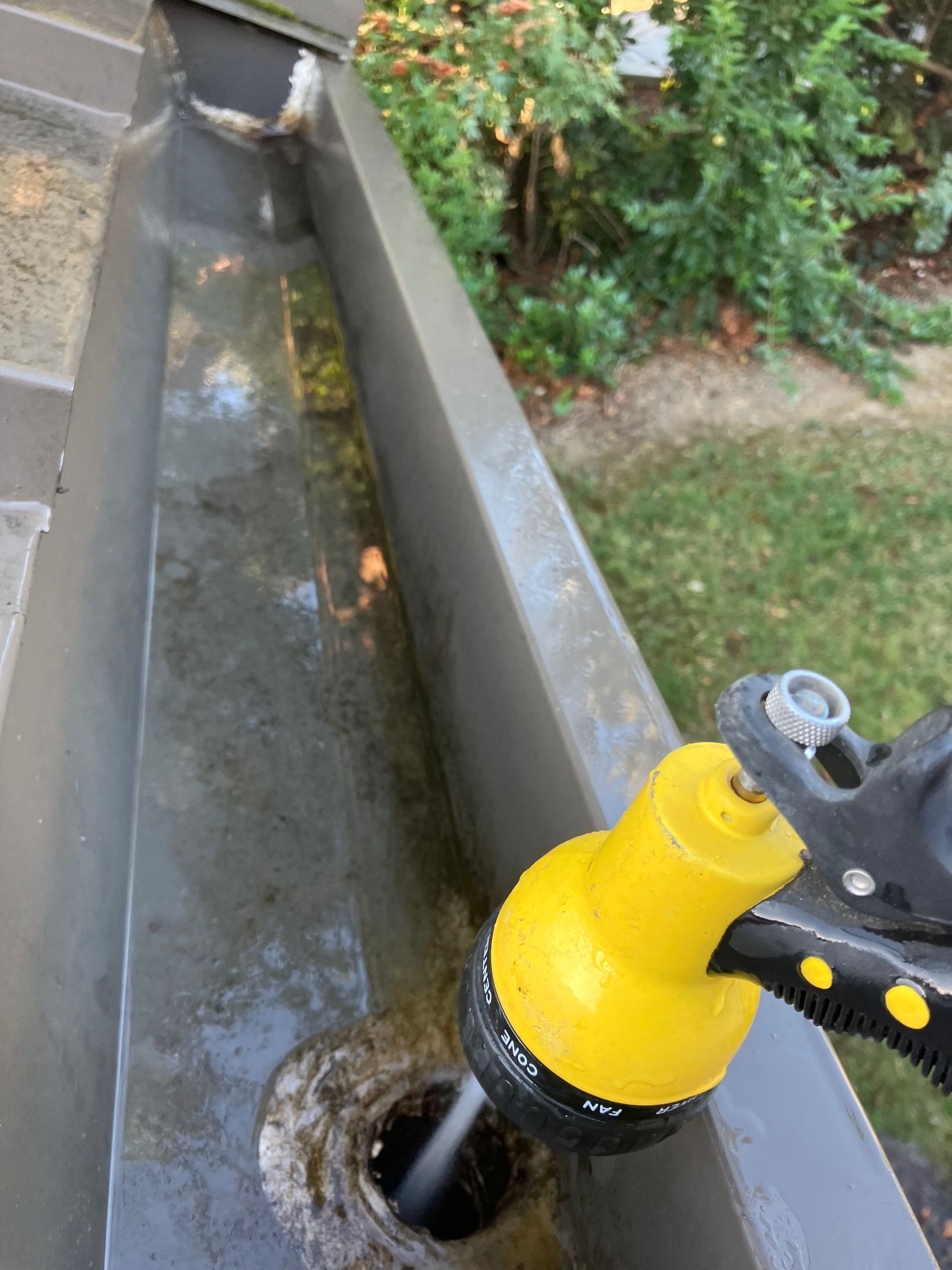 Person cleaning a gutter with a yellow nozzle, water spraying down.