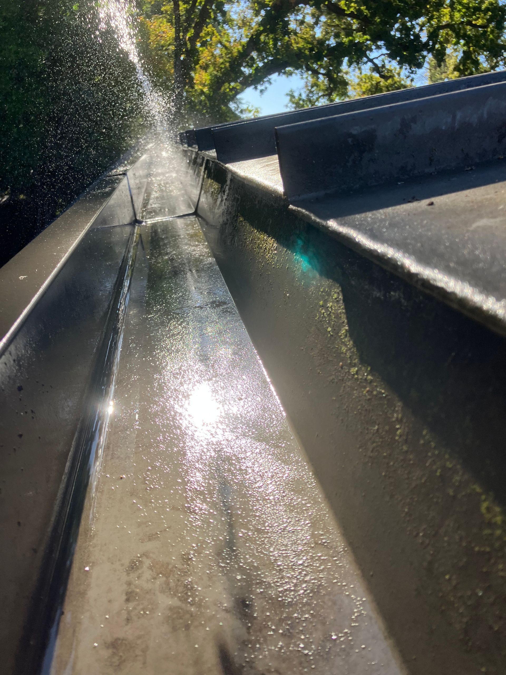 Cleaning a gutter with water, sunlight glinting.