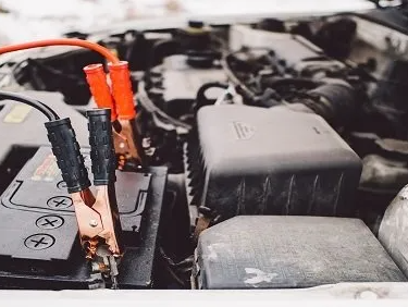 Car engine with jumper cables connected to a battery, boosting power.