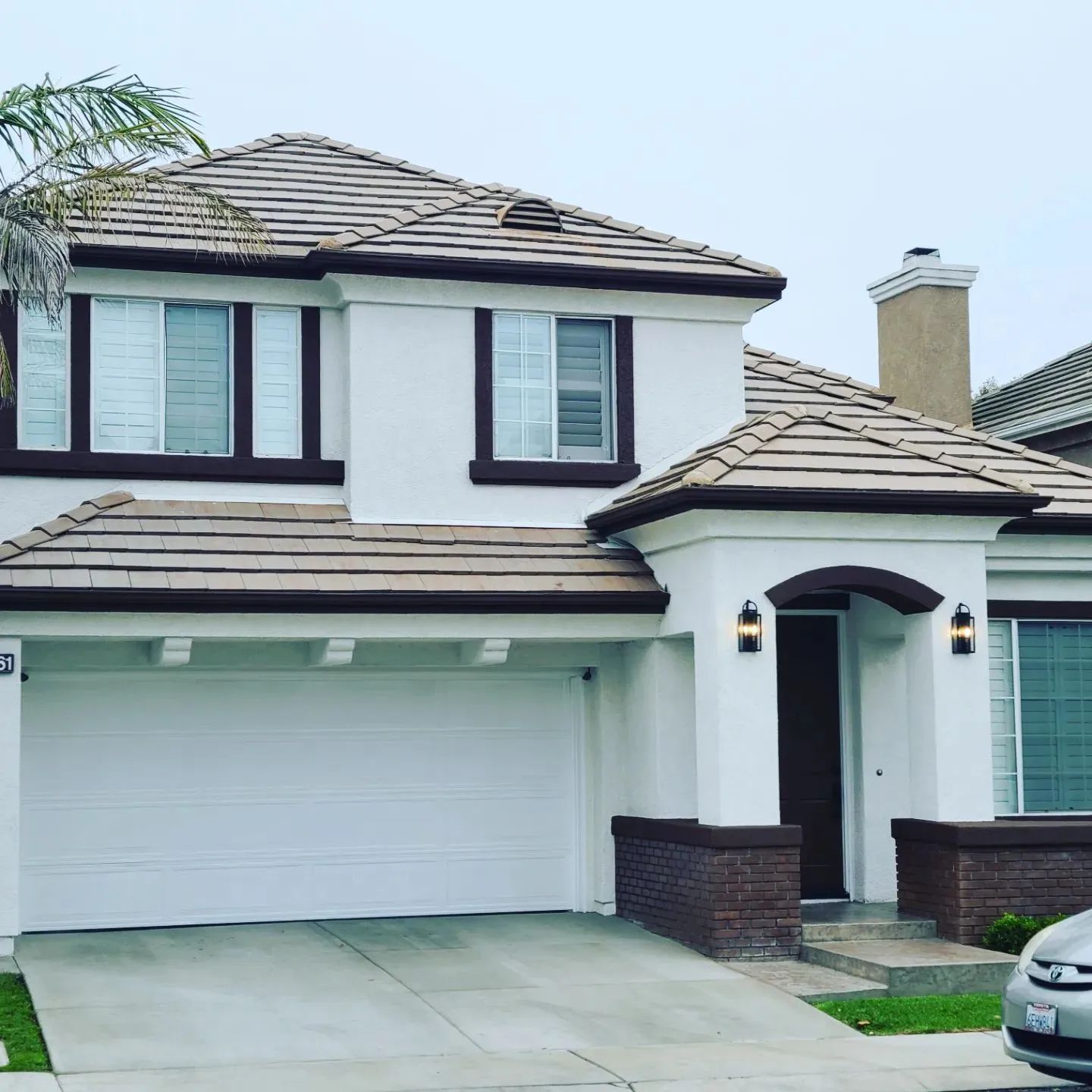 A two-story house with white stucco walls, brown trim, a tiled roof, and an attached two-car garage.