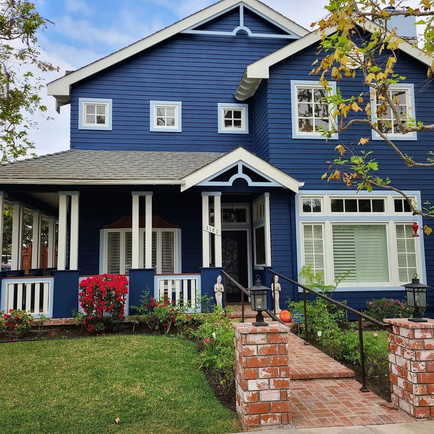 A two-story navy blue house with white trim, a wrap-around front porch, and a brick walkway leading to the entrance.