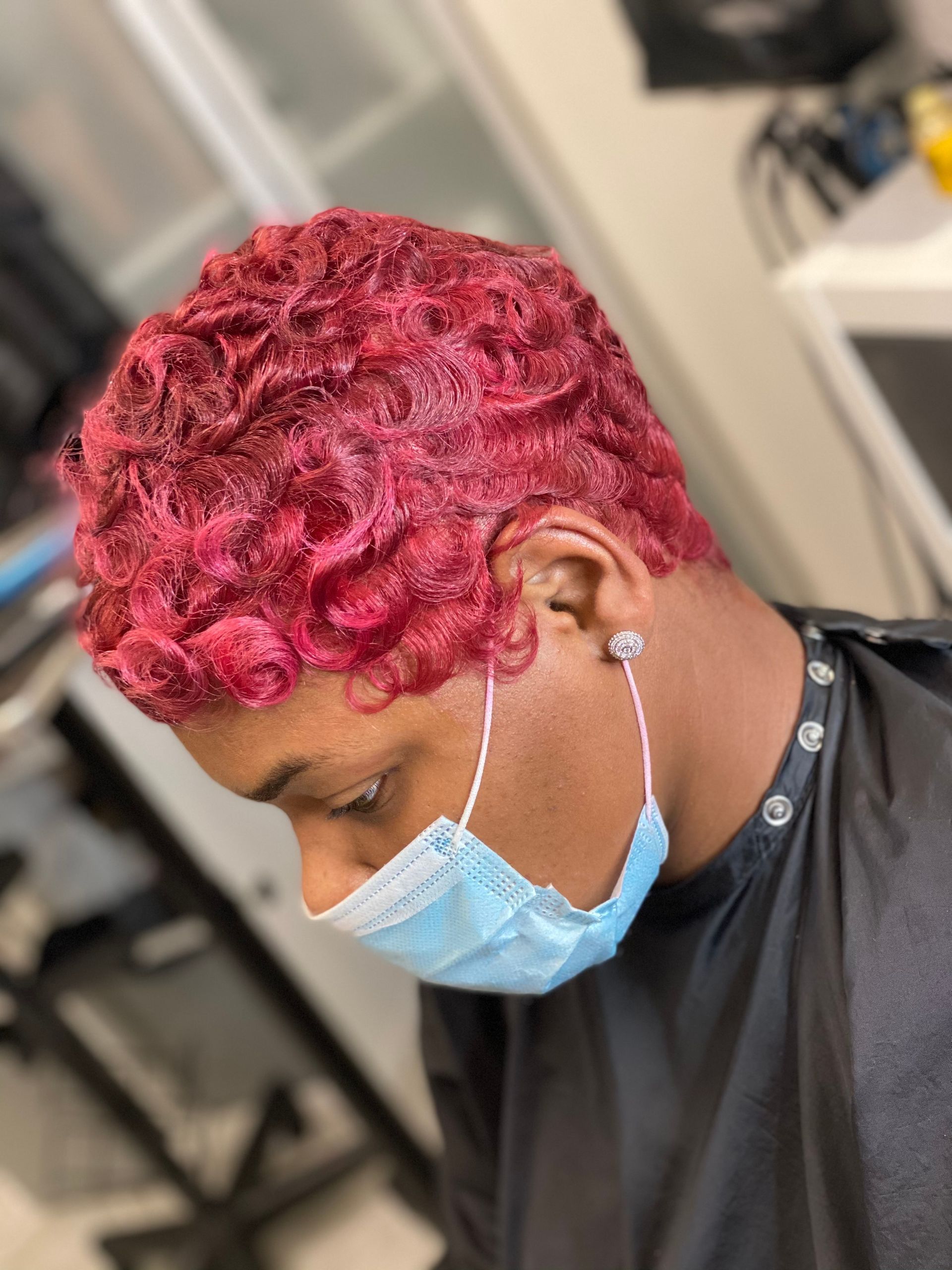 A stylist applying hair dye with a brush and foil to a client's dark hair in a salon.
