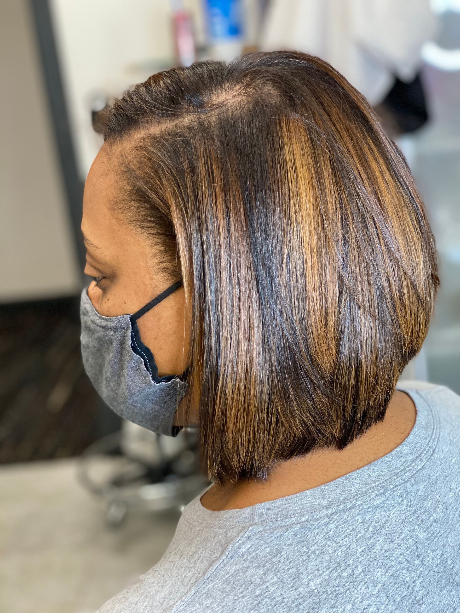 Woman with a shoulder-length bob hairstyle, wearing a gray mask and sweater. Her hair is brown with blonde highlights.