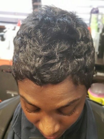 Woman with short, wavy black hair, eyes closed, wearing a salon cape.