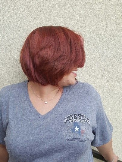 Woman with auburn bob haircut, smiling, wearing a gray Texas-themed t-shirt, against a beige wall.