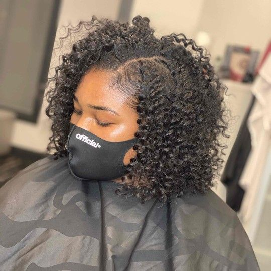 Woman with dark curly hair and a black mask, indoors.