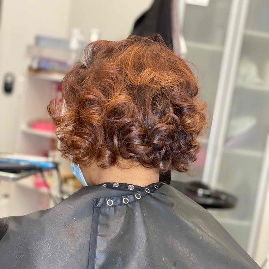 Woman with curly auburn hair, wearing a salon cape, in a beauty salon.