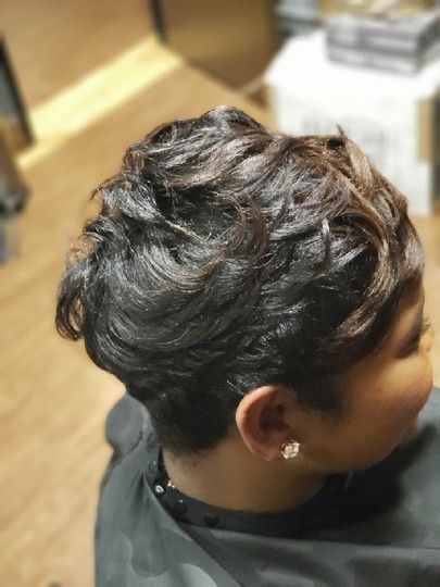 Woman with short, dark, wavy hair at a salon. Side view shows a hint of her face and ear.