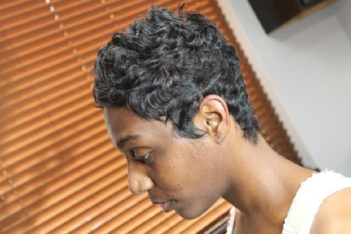 Woman with short, dark, curly hair looking down near a window with blinds.
