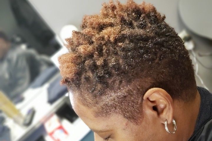 Person with short, curly brown hair, shaved sides, wearing hoop earrings, head tilted down.