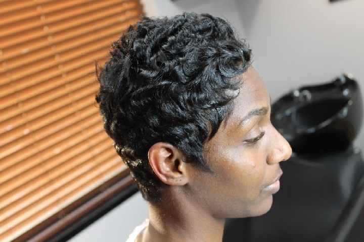 Woman with short, wavy black hair, profile view in a salon setting.