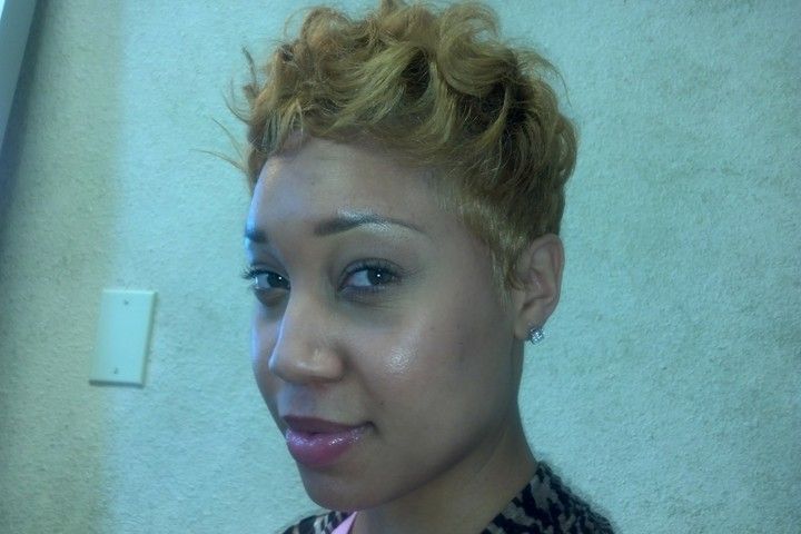 Woman with short, curly blonde hair, looking towards the camera. She's in a room with a light wall.