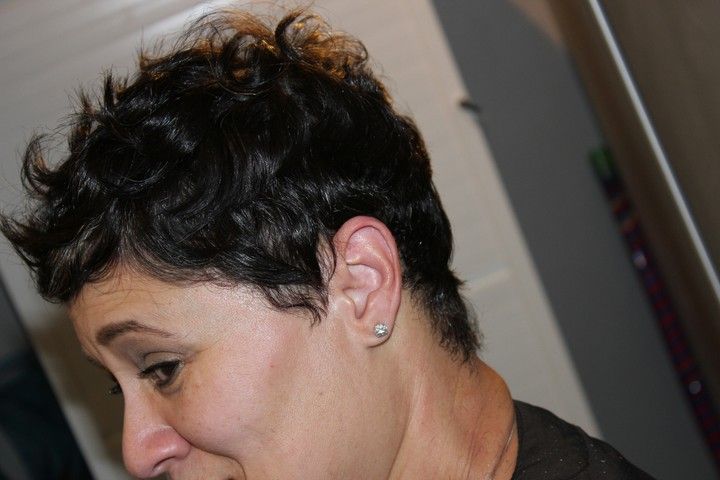 Woman with short, dark, curly hair; looking to the left, small diamond earring.