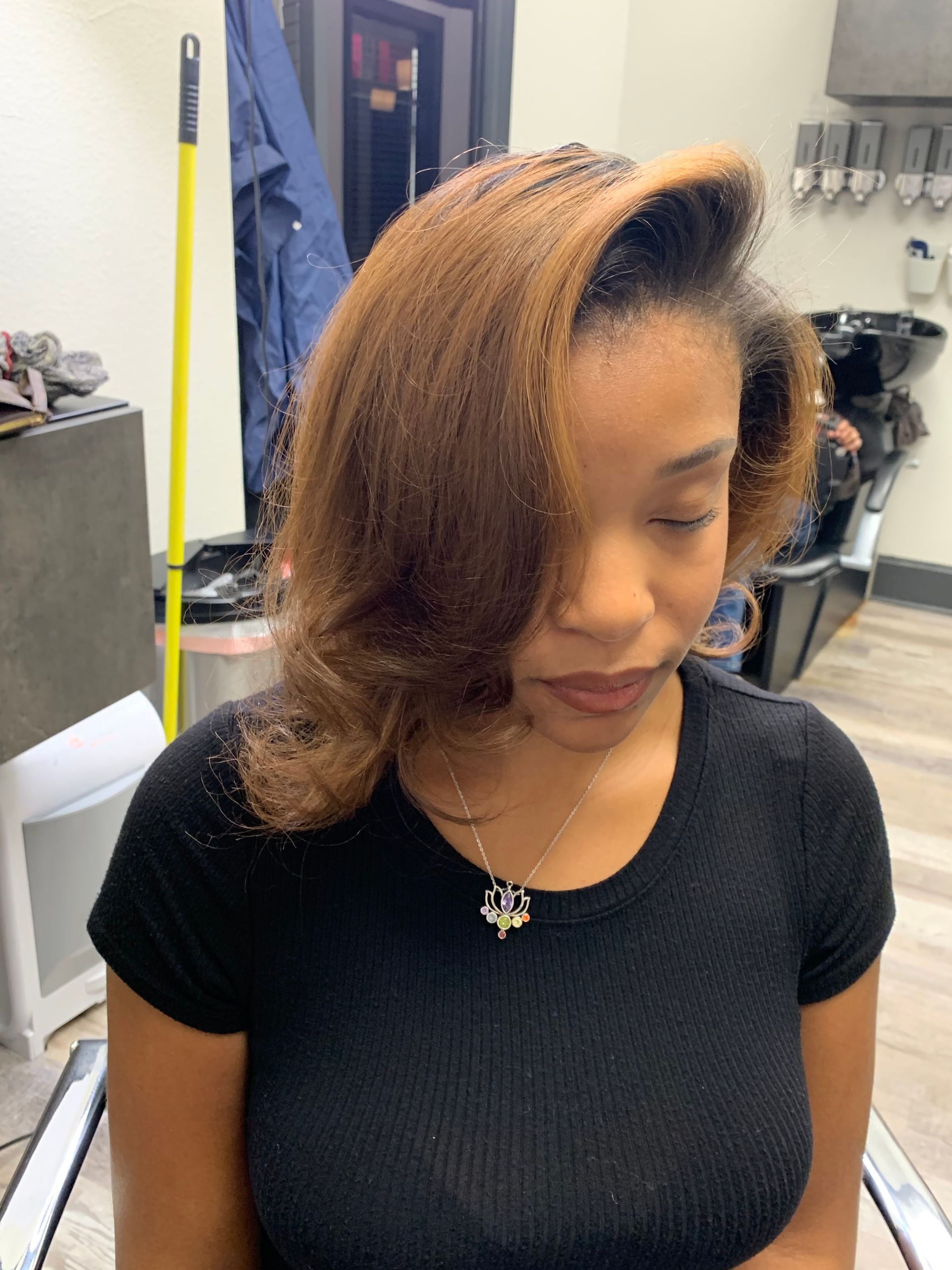 Woman with brown hair styled in a salon, wearing a black shirt, and a necklace.