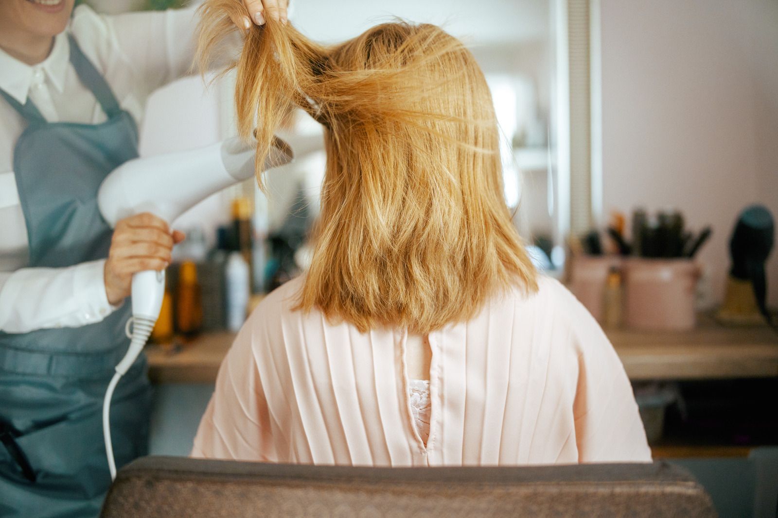 Hairdresser blow-drying a client's blonde hair in a salon, close up.