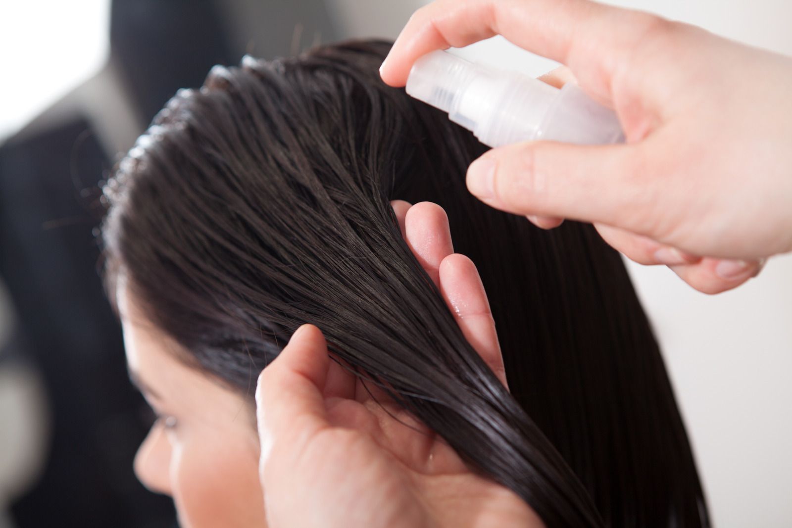 Person spraying hair with a clear bottle; salon setting.