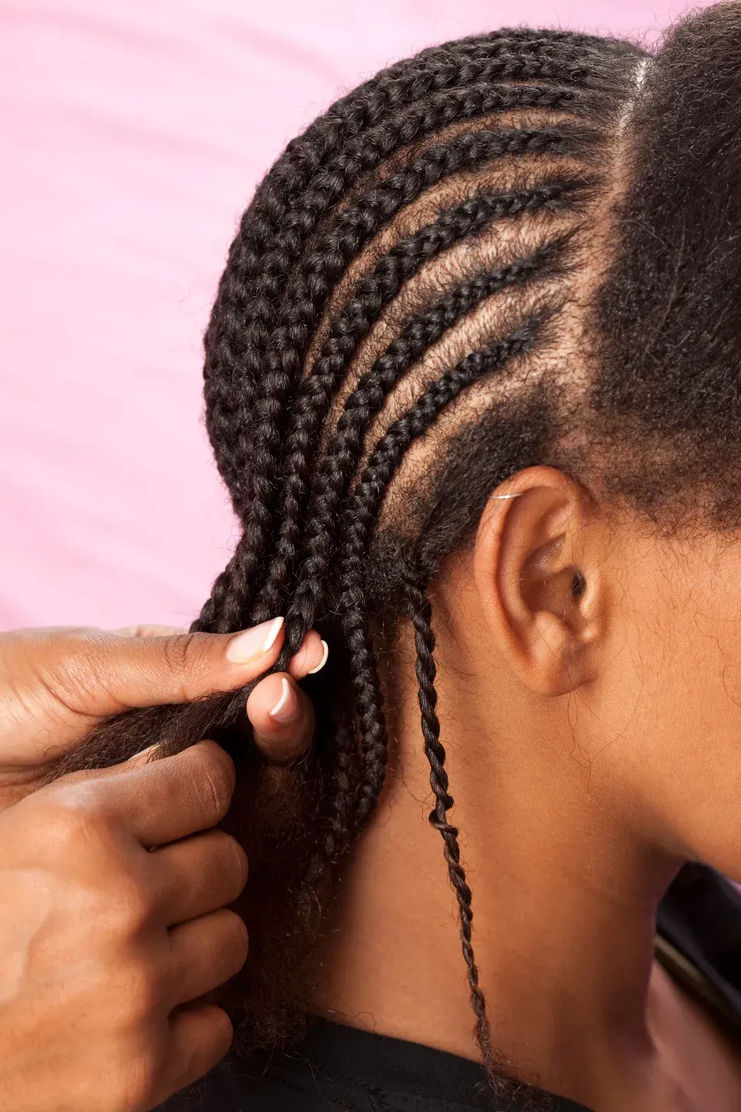 Hands braiding dark hair close-up; braids styled near the head.