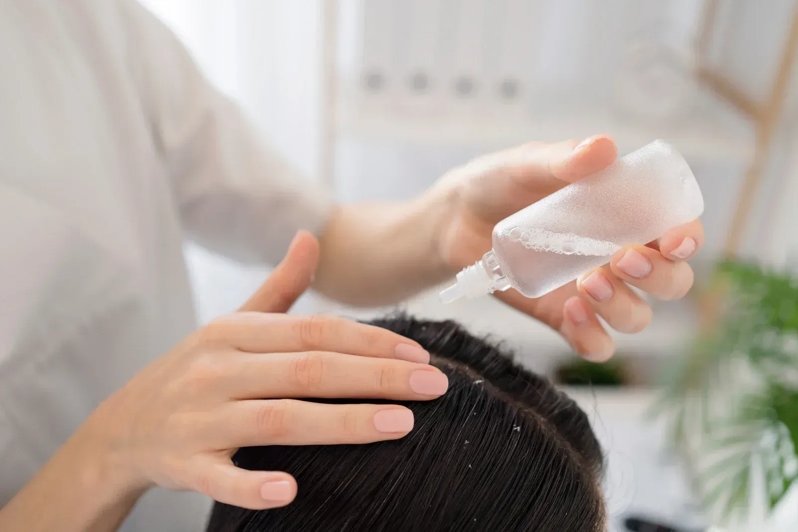 Person applying a product to someone's scalp, possibly for hair treatment, in a bright indoor setting.