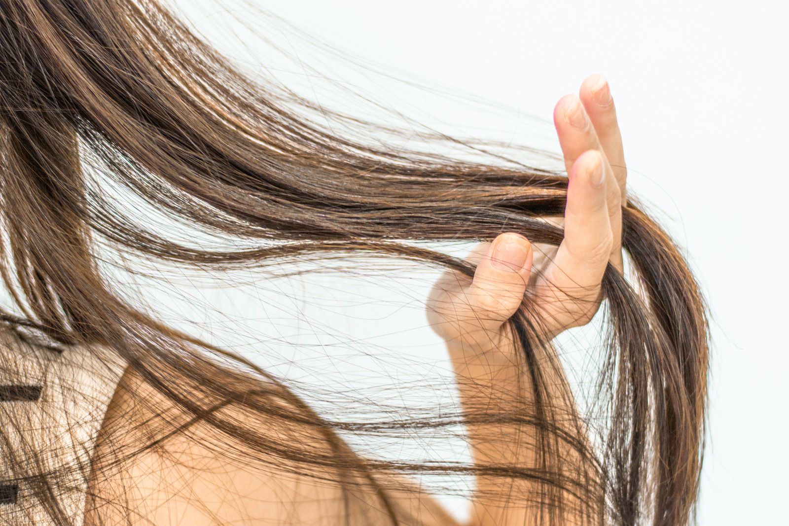 Hand holding and inspecting flowing brown hair against a white background.
